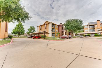 A parking lot in front of apartment buildings with a red car parked in the lot at Limestone Ranch Apartments, Lewisville, Texas